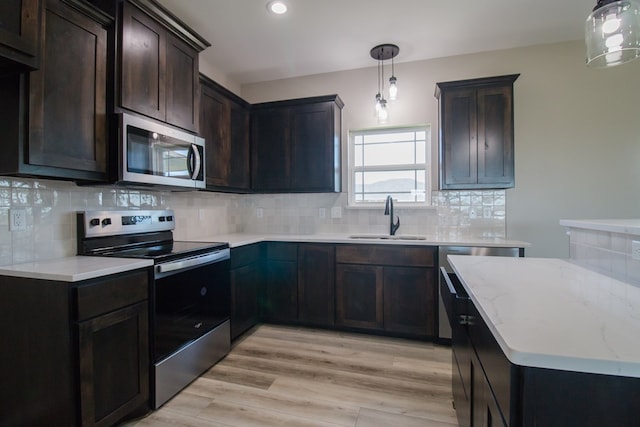 kitchen with sink, decorative backsplash, hanging light fixtures, light hardwood / wood-style floors, and stainless steel appliances