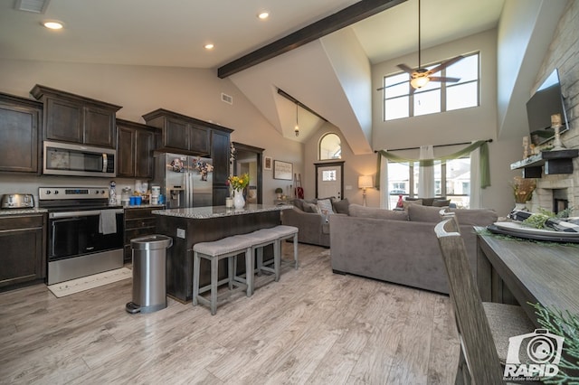 kitchen with open floor plan, a kitchen bar, appliances with stainless steel finishes, light wood-style floors, and a ceiling fan