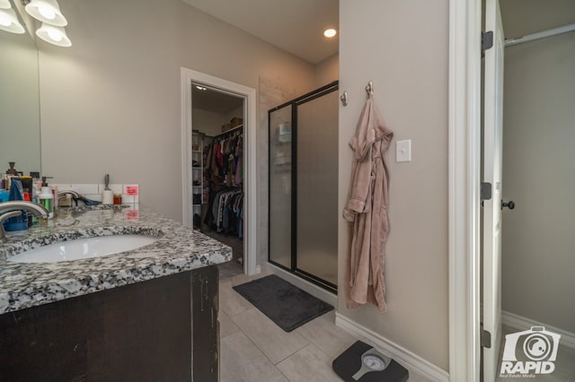 bathroom featuring a walk in closet, tile patterned floors, vanity, and a stall shower