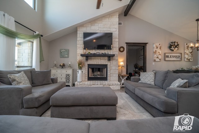 living area featuring beamed ceiling, high vaulted ceiling, a stone fireplace, and ceiling fan with notable chandelier