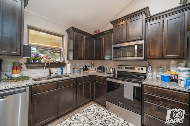 kitchen with light stone countertops, lofted ceiling, a sink, dark brown cabinets, and appliances with stainless steel finishes