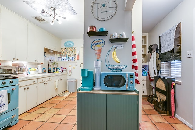 kitchen featuring stove, pendant lighting, white cabinets, and light tile patterned flooring