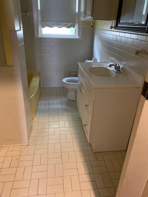 217 S Monroe St, San Angelo, TX 76901 - full bath with toilet, vanity, a tub, tile patterned flooring, and tile walls
