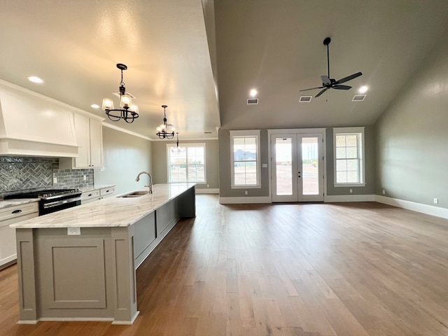 kitchen featuring sink, wall chimney range hood, white cabinetry, stainless steel range with gas stovetop, and a large island with sink