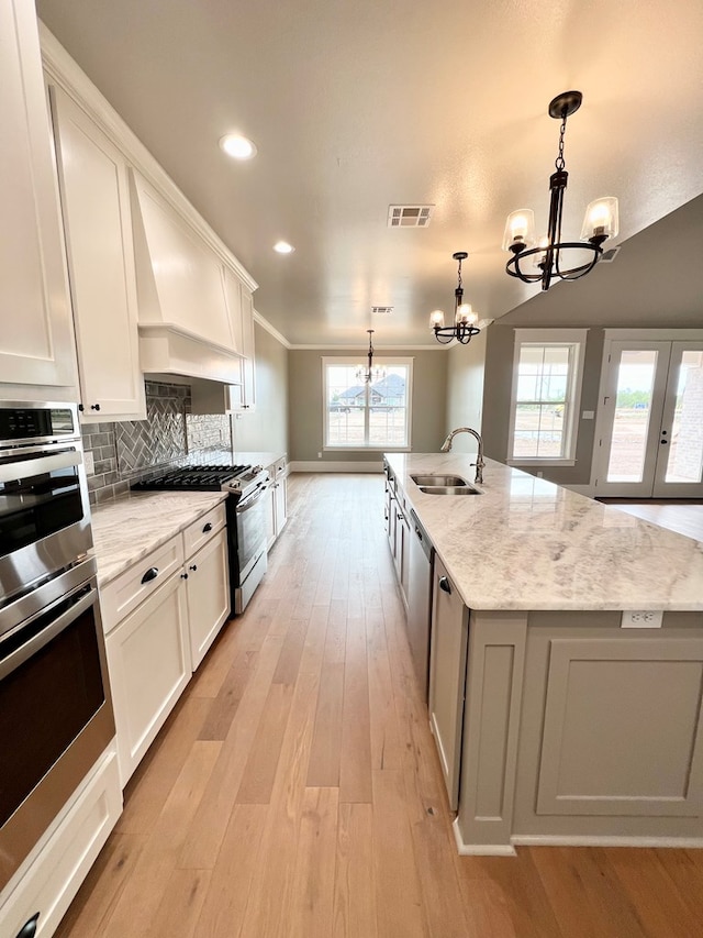 kitchen featuring premium range hood, sink, hanging light fixtures, a kitchen island with sink, and white cabinets