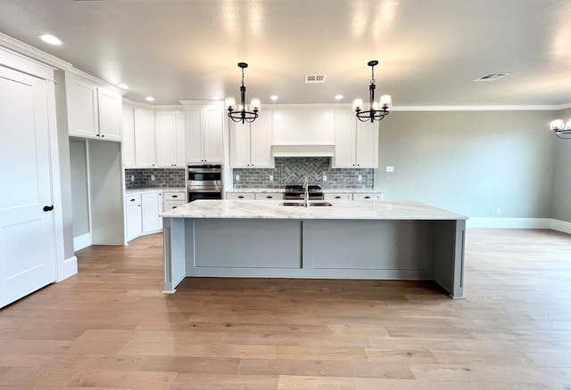 kitchen featuring white cabinetry, hanging light fixtures, light stone countertops, an island with sink, and a chandelier