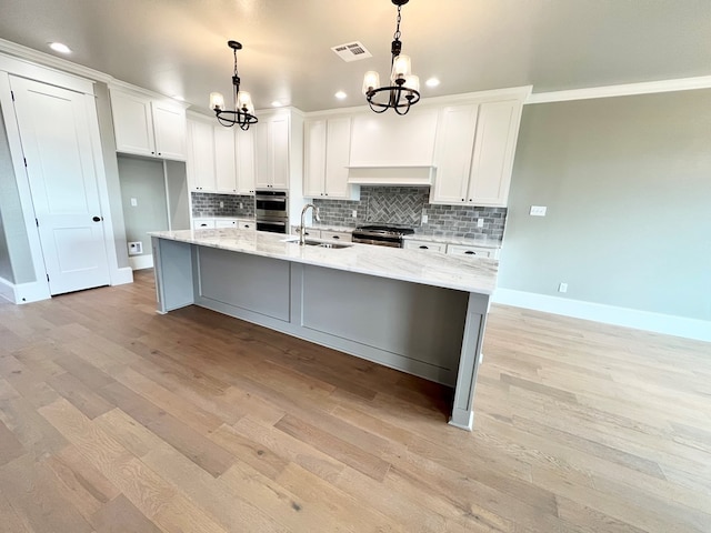 kitchen featuring appliances with stainless steel finishes, decorative light fixtures, sink, white cabinets, and a kitchen island with sink