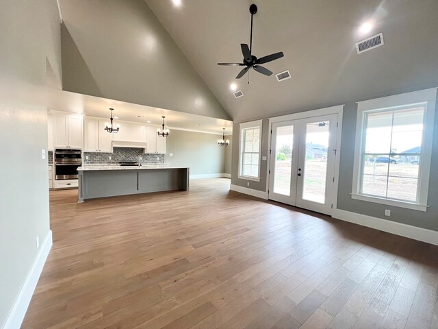 unfurnished living room with ceiling fan with notable chandelier, high vaulted ceiling, and light wood-type flooring