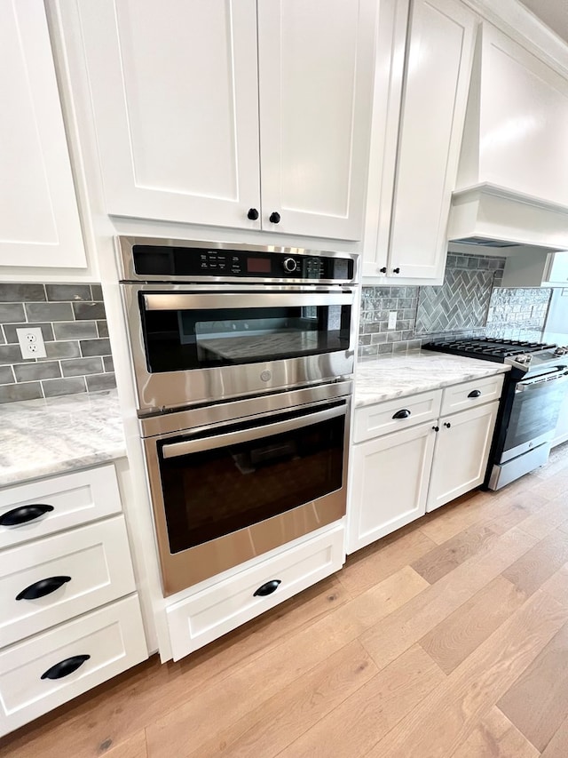 kitchen with white cabinetry, backsplash, stainless steel appliances, light stone counters, and light wood-type flooring