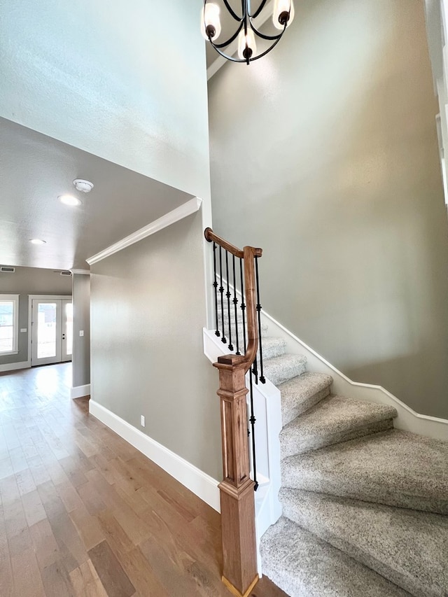 stairs with a high ceiling, wood-type flooring, an inviting chandelier, and crown molding