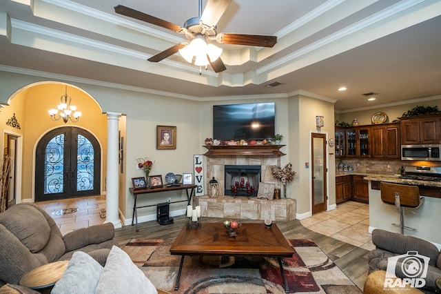 living room with a fireplace, decorative columns, ornamental molding, a raised ceiling, and french doors