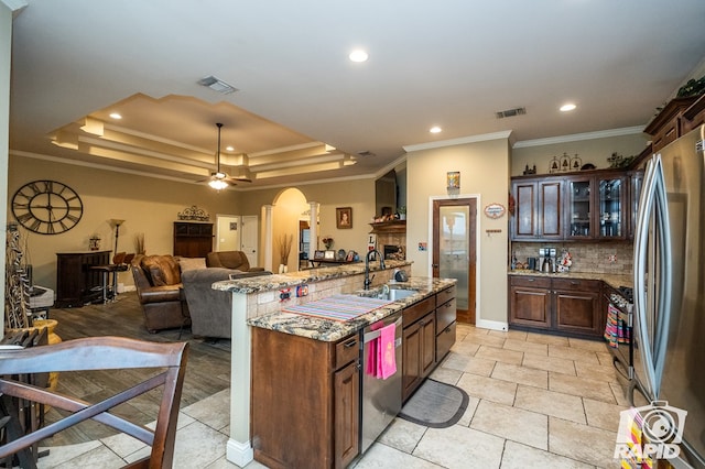 kitchen with sink, dark brown cabinets, a raised ceiling, an island with sink, and stainless steel appliances