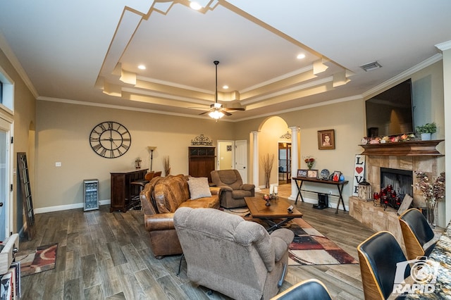 living room with ornamental molding, dark hardwood / wood-style floors, a raised ceiling, ceiling fan, and a tiled fireplace