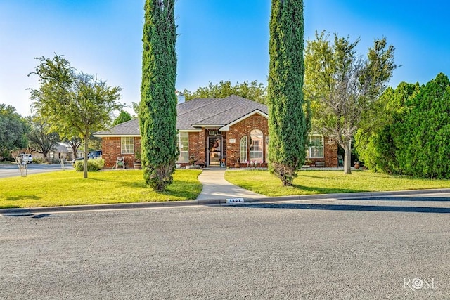 ranch-style house featuring brick siding, a chimney, a front yard, and roof with shingles