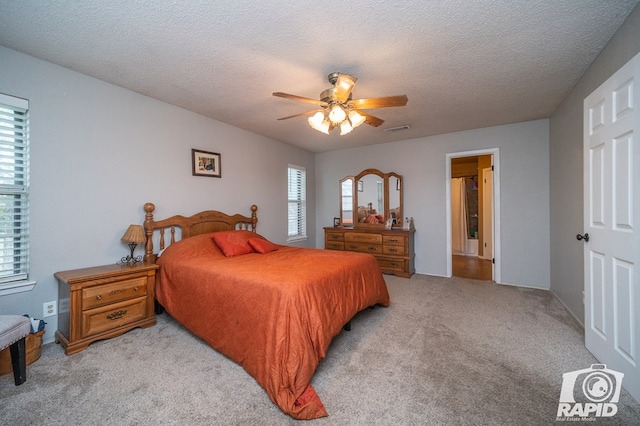 bedroom featuring visible vents, light colored carpet, a textured ceiling, and ceiling fan