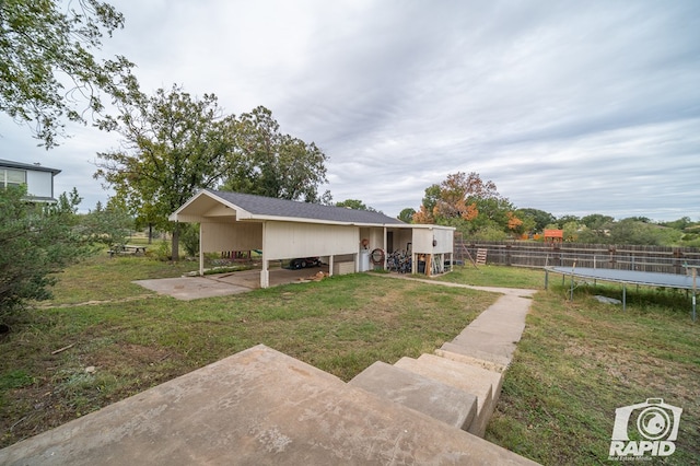 back of property featuring a carport, a trampoline, fence, and a lawn
