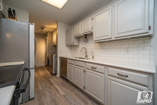 kitchen featuring backsplash, stainless steel dishwasher, washer and dryer, a sink, and wood finished floors