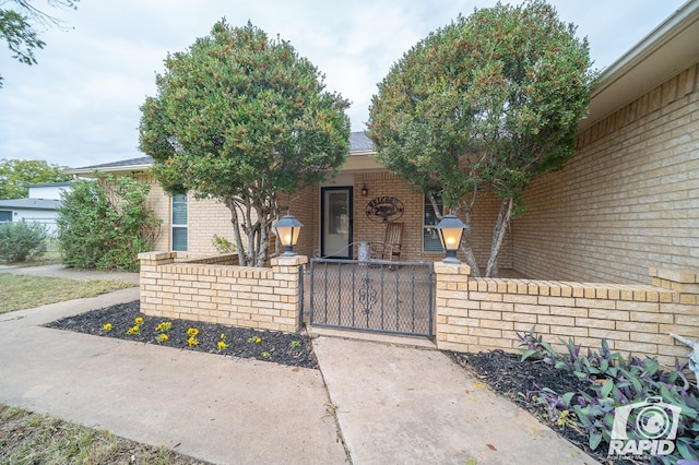 property entrance featuring brick siding, a porch, fence, and a gate
