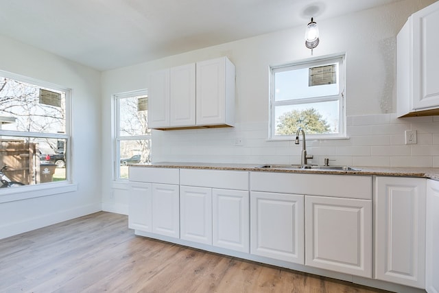 kitchen with sink, stone counters, white cabinetry, backsplash, and light wood-type flooring