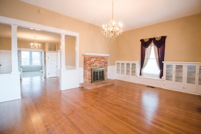 unfurnished living room featuring hardwood / wood-style flooring, a chandelier, a brick fireplace, and ornate columns