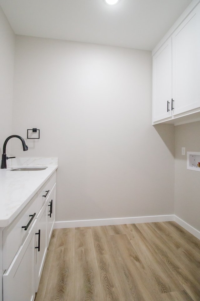 clothes washing area featuring light wood-style floors, cabinet space, a sink, and baseboards