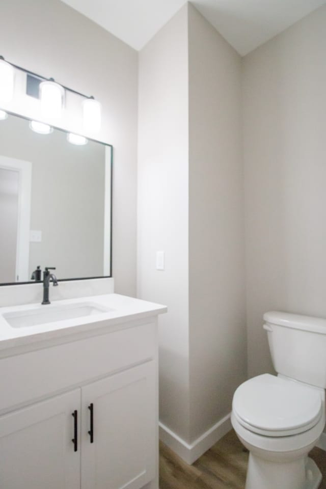 bathroom with toilet, baseboards, wood finished floors, and vanity