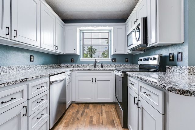 kitchen with a sink, a textured ceiling, appliances with stainless steel finishes, and wood finished floors