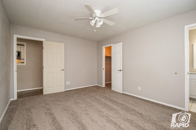 unfurnished bedroom with a spacious closet, baseboards, carpet flooring, a closet, and ensuite bath