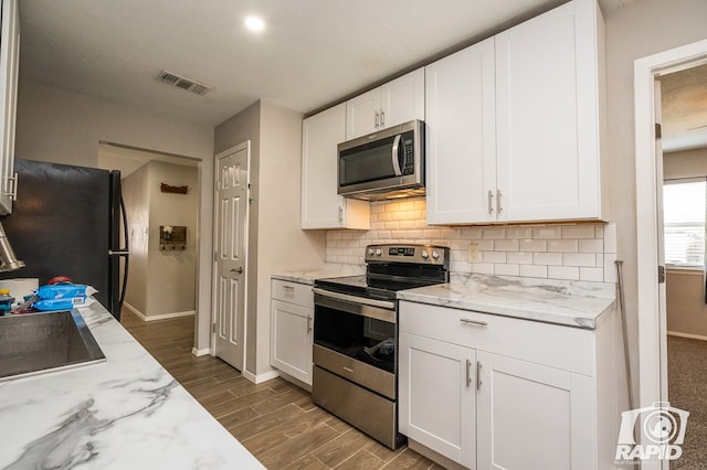 kitchen with wood finish floors, visible vents, tasteful backsplash, white cabinetry, and appliances with stainless steel finishes