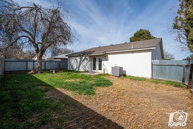 rear view of property featuring a lawn, central AC, and a fenced backyard