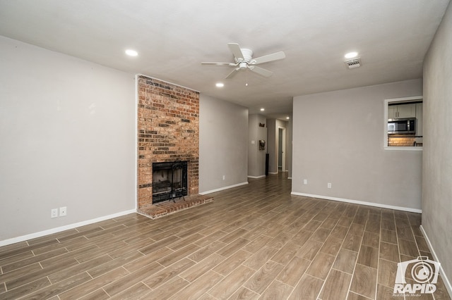 unfurnished living room featuring visible vents, wood finished floors, a brick fireplace, and ceiling fan