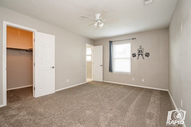 unfurnished bedroom with a walk in closet, baseboards, visible vents, and carpet floors