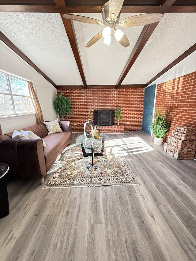 living room with wood-type flooring, brick wall, vaulted ceiling with beams, and a textured ceiling