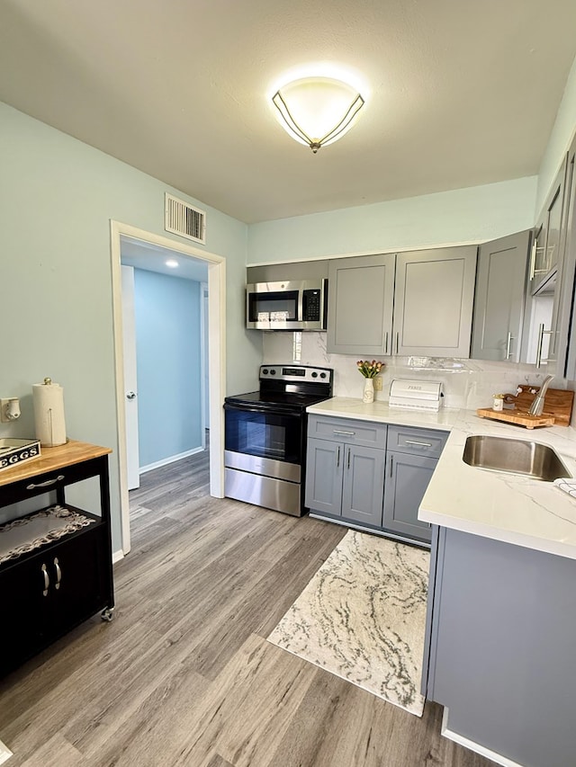 kitchen featuring light wood-type flooring, sink, gray cabinets, and appliances with stainless steel finishes