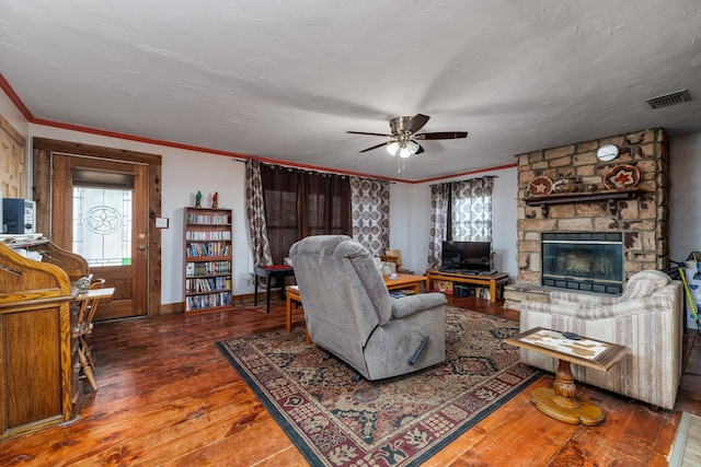 living room with a stone fireplace, crown molding, a textured ceiling, dark hardwood / wood-style floors, and ceiling fan