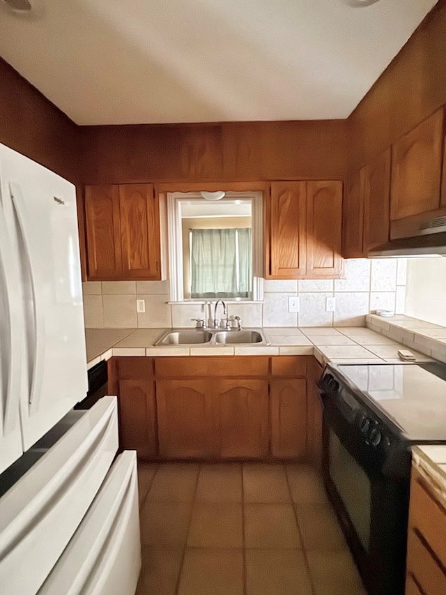 kitchen featuring black stove, sink, white refrigerator, light tile patterned floors, and tile counters