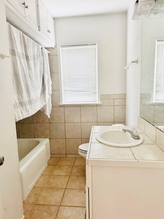 bathroom with tile walls, a bathtub, tile patterned flooring, vanity, and toilet