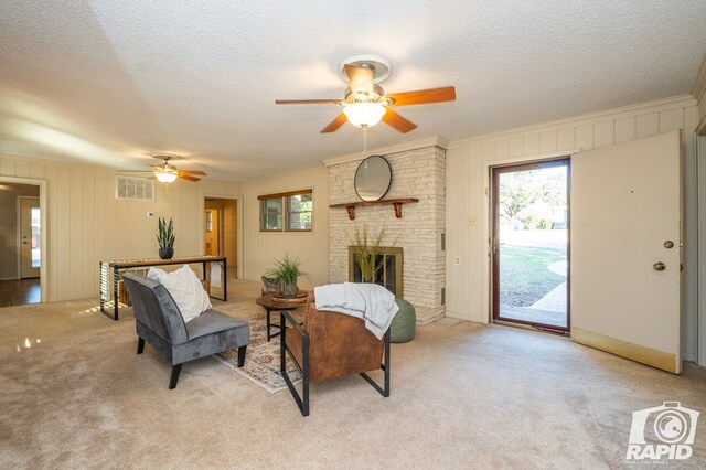 living room featuring light colored carpet, a textured ceiling, ornamental molding, ceiling fan, and a fireplace