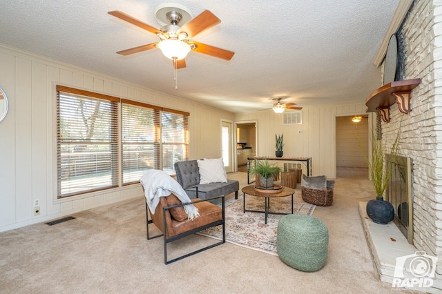 living room with ceiling fan, a brick fireplace, light colored carpet, and a textured ceiling