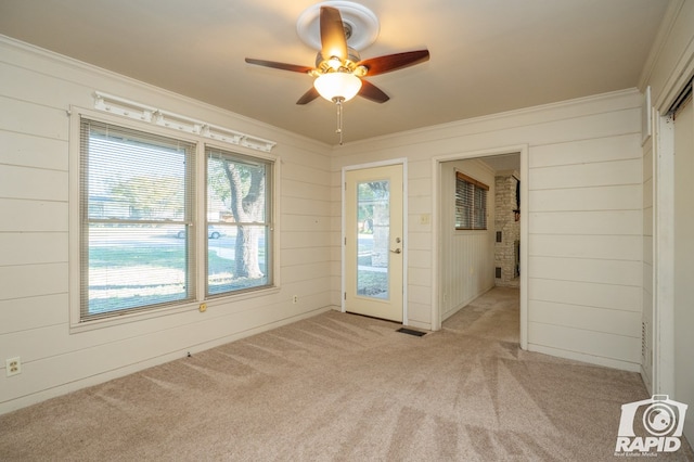 unfurnished room with ceiling fan, light colored carpet, wooden walls, and crown molding