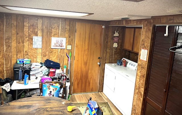 laundry area featuring washing machine and dryer, a textured ceiling, wooden walls, and light wood-style flooring