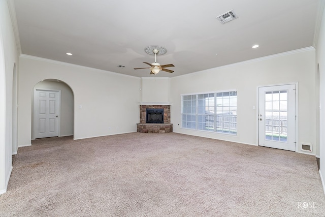 unfurnished living room featuring ornamental molding, a stone fireplace, light colored carpet, and ceiling fan