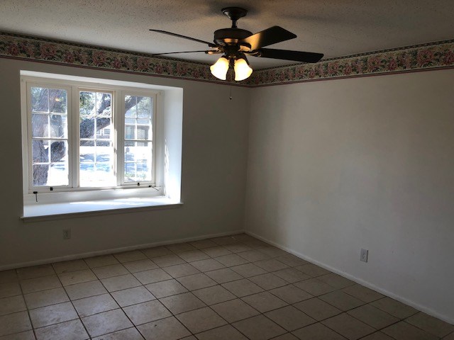 unfurnished room featuring baseboards, a textured ceiling, ceiling fan, and light tile patterned floors