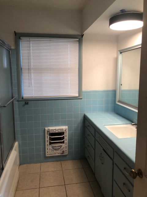 full bathroom featuring heating unit, vanity, enclosed tub / shower combo, tile patterned flooring, and tile walls