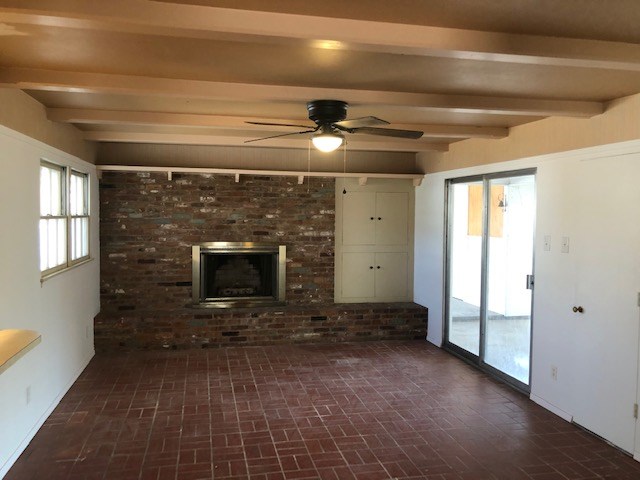 unfurnished living room with a fireplace, beamed ceiling, brick floor, and a ceiling fan