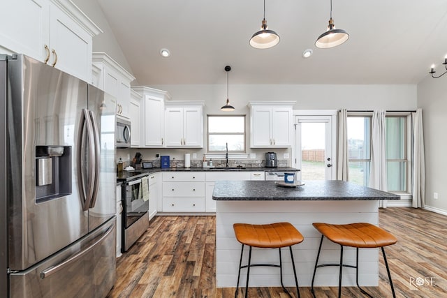 kitchen featuring sink, hanging light fixtures, stainless steel appliances, white cabinets, and vaulted ceiling