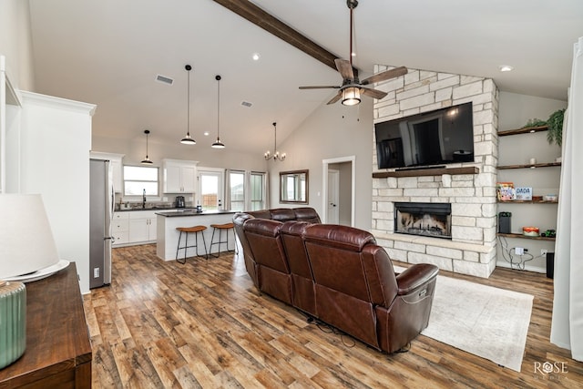 living room with sink, hardwood / wood-style flooring, a fireplace, ceiling fan with notable chandelier, and beamed ceiling