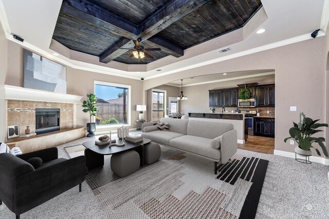 carpeted living room featuring coffered ceiling, ornamental molding, a raised ceiling, beam ceiling, and a tiled fireplace