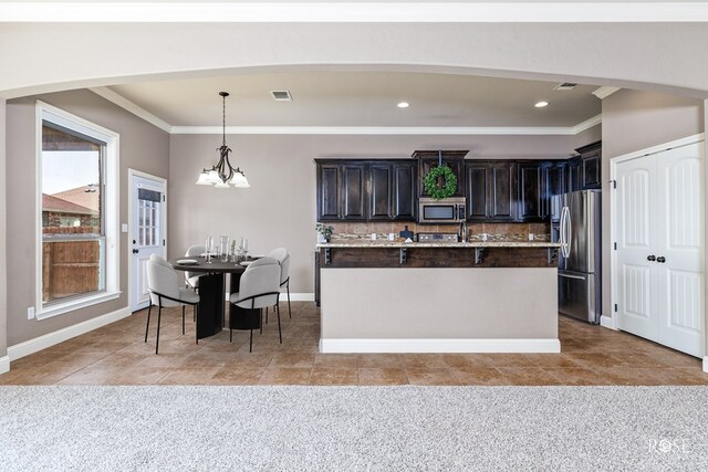 kitchen featuring appliances with stainless steel finishes, tasteful backsplash, an island with sink, light carpet, and decorative light fixtures