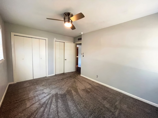 unfurnished bedroom with two closets, ceiling fan, and carpet flooring